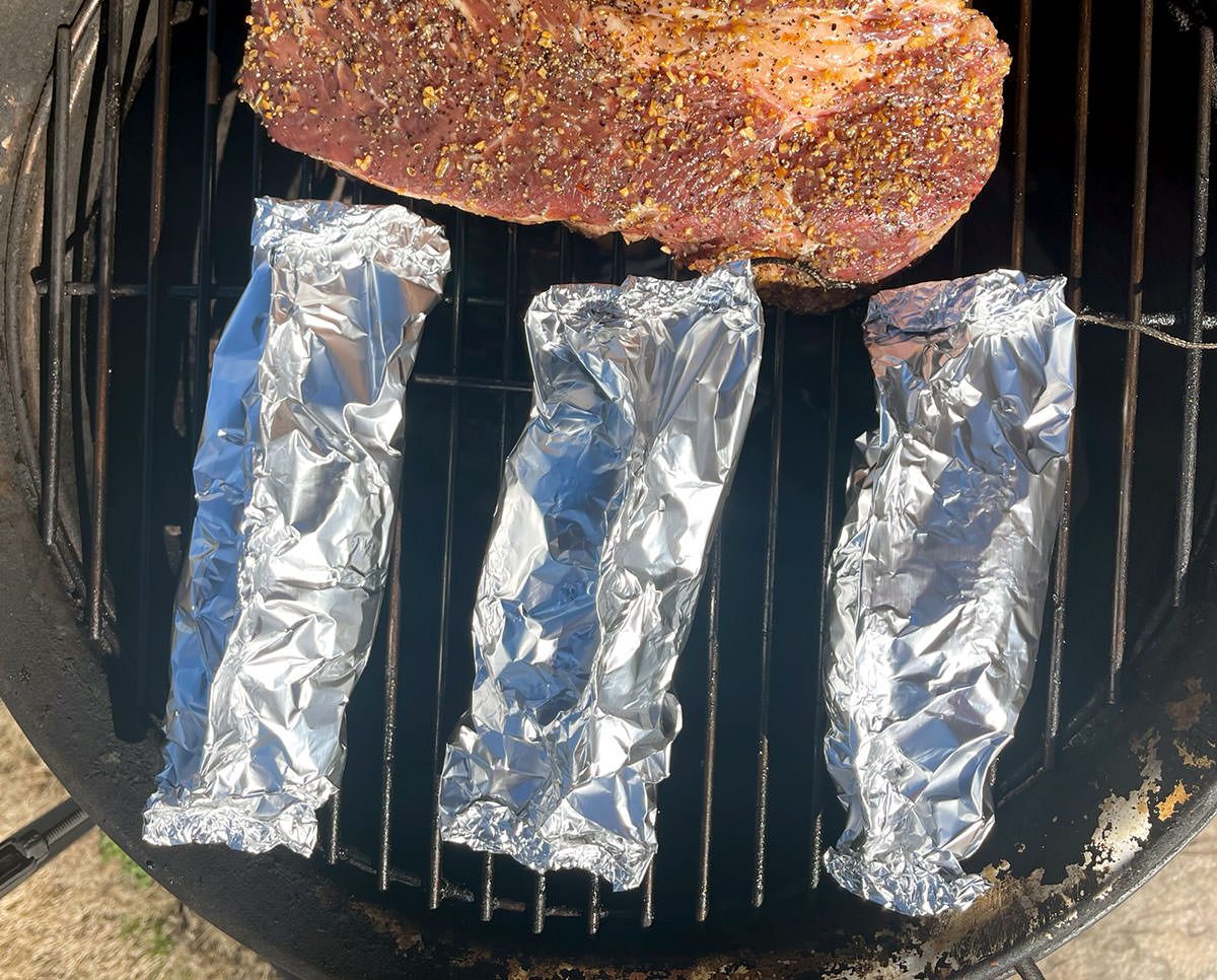 Foil wrapped baked potatoes on a smoker.