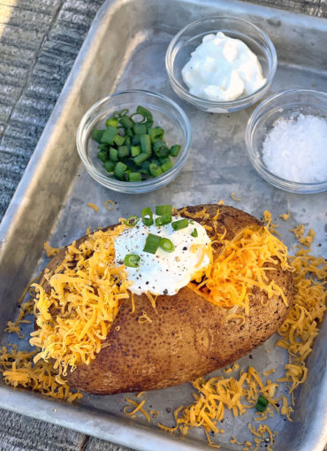 Smoked baked potatoes and baked potato toppings on a silver baking sheet.