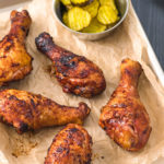 Smoked chicken legs on a silver baking sheet lined with parchment paper.