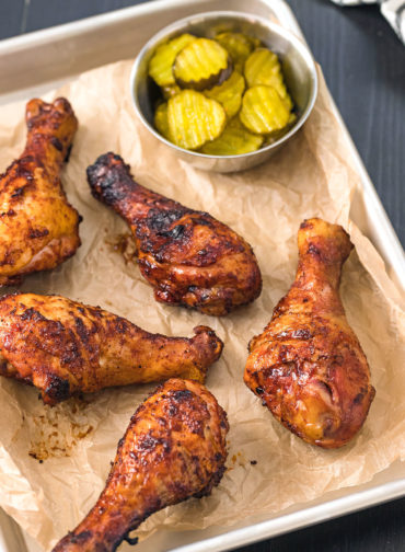 Smoked chicken legs on a silver baking sheet lined with parchment paper.