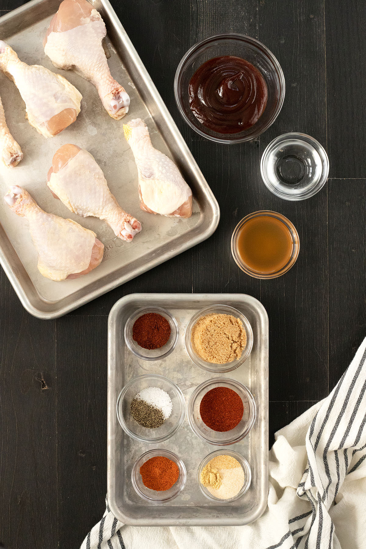 Raw chicken and spices on silver baking sheets.