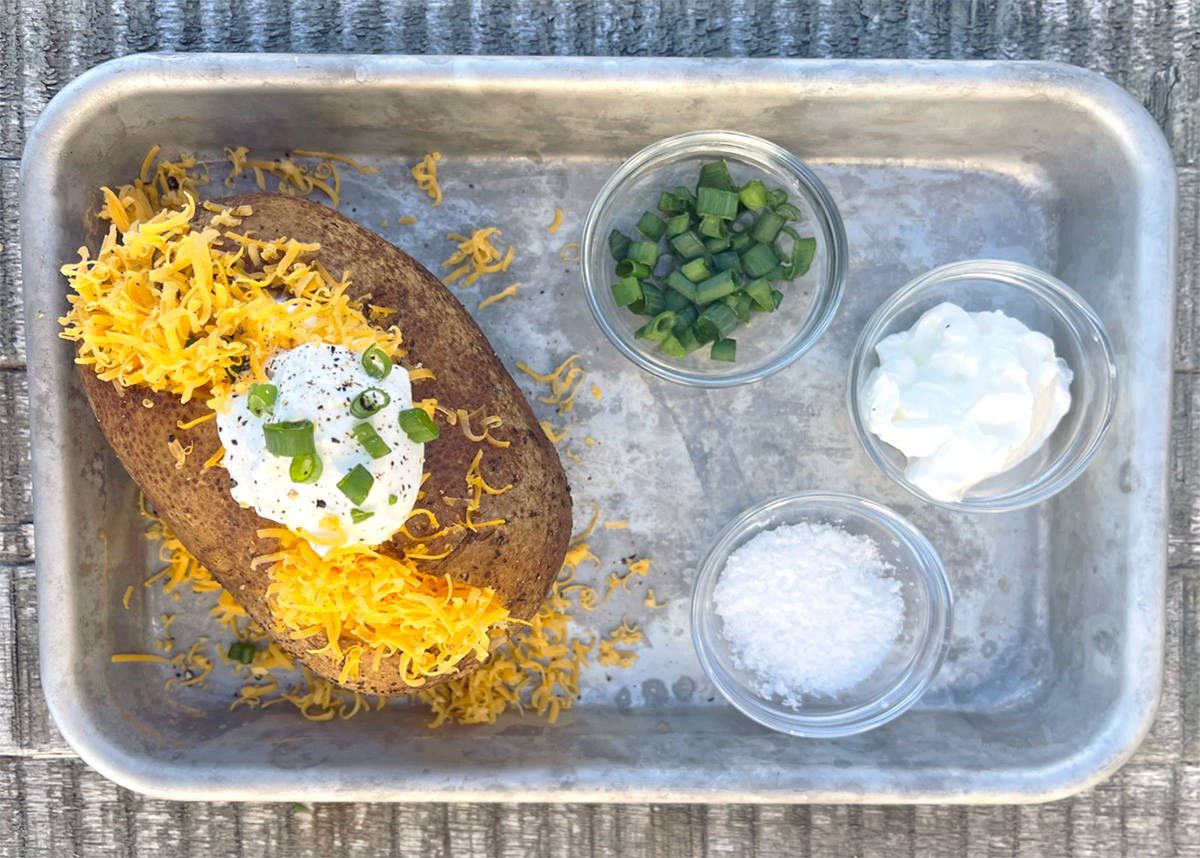 Baked potato topped with cheese and sour cream on a baking sheet.